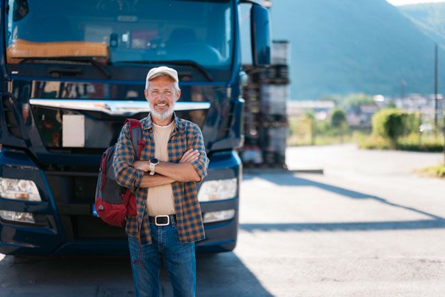 A truck driver happily stands in front of a truck.