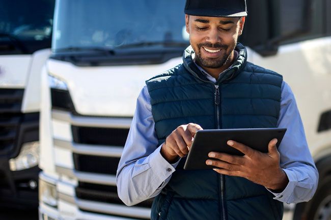 A fleet manager reviews fleet card usage on his tablet outside by his fleet of vehicles.