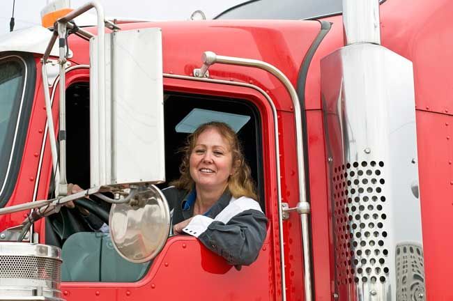 A truck driver smiles out her rig window while at a stop.