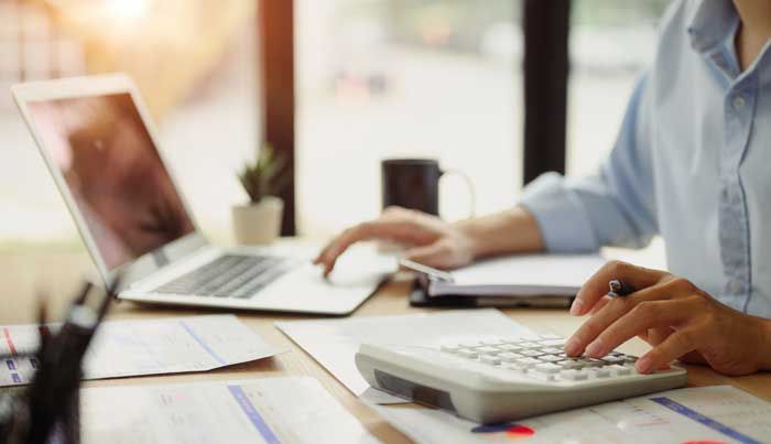 A business accountant working through paperwork using their laptop and calculator.